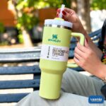 A woman holding a lime green Stanley Quencher H2.0 Tumbler with a straw while sitting on a park bench.