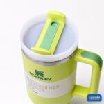 A woman holding a lime green Stanley Quencher H2.0 Tumbler with a straw while sitting on a park bench. - view 2
