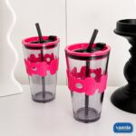A hand holding a smoked grey Hoho Glass Sipper with a bright pink silicone bubble grip and matching lid. - view 2