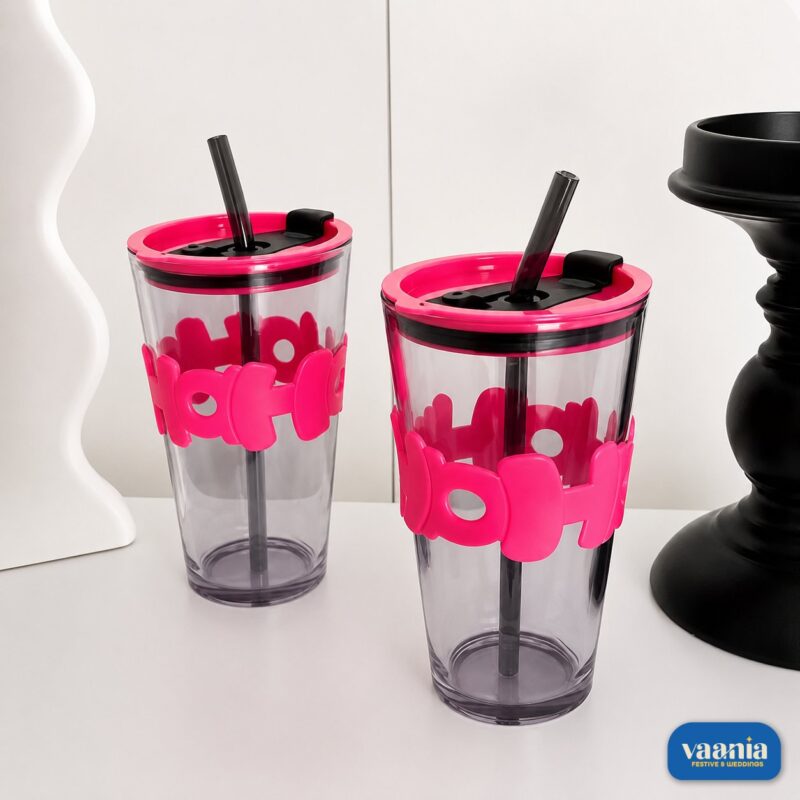 A hand holding a smoked grey Hoho Glass Sipper with a bright pink silicone bubble grip and matching lid. - view 2