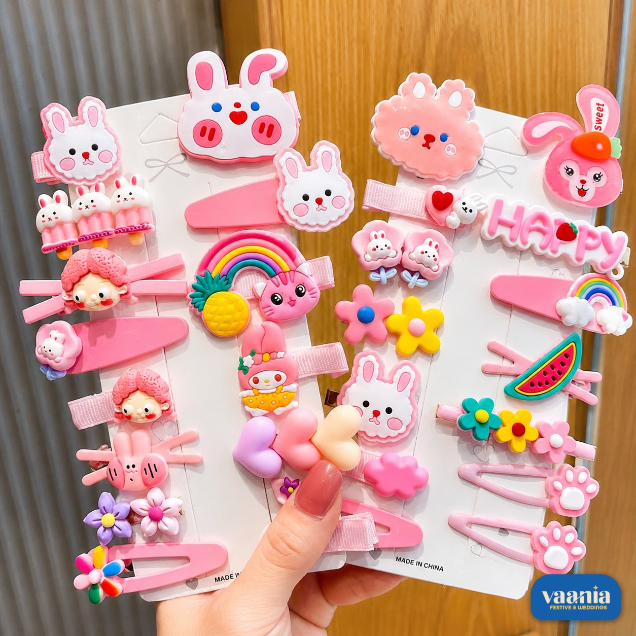 Sweet Charm Hair Clips Set by Vaania A hand holding three cards of pink Sweet Charm Hair Clips featuring rabbits, rainbows, and flowers.