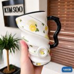 Two Fruity Ceramic Mugs with cherry and lemon patterns featuring spiral ridges and black wavy handles held by hands. - view 2