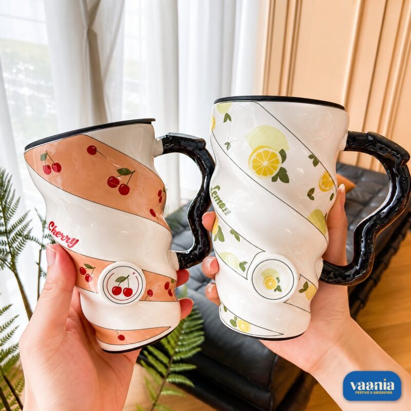 Two Fruity Ceramic Mugs with cherry and lemon patterns featuring spiral ridges and black wavy handles held by hands.