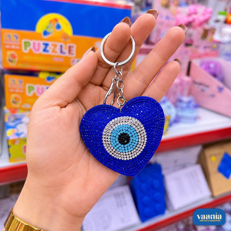 Two heart-shaped Evil Eye Keychains in black and blue being held by a hand showing crystal details. - view 2