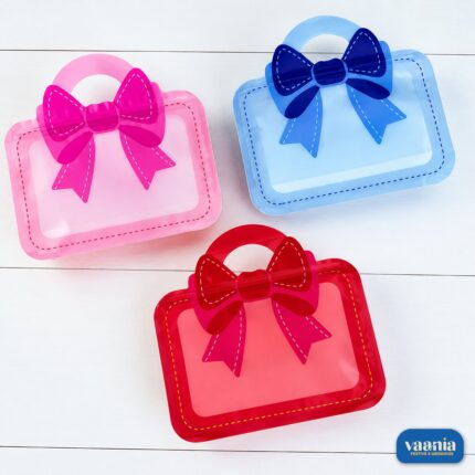 Three Bow Hamper Pouches in pink, blue, and red colors with large bow designs on a white wooden surface.
