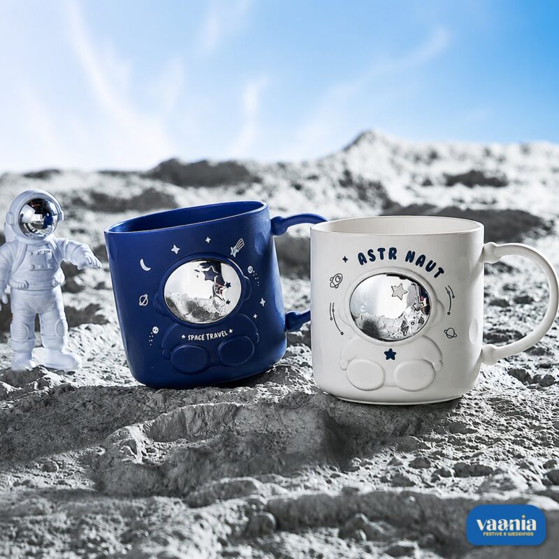 Blue and white Astronaut Buddy Mugs holding toothbrushes on a cream tray in a bathroom setting. - view 2