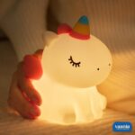 A glowing Sitting Unicorn Silicone Night Lamp with a colorful horn and pink wings on a pink background. - view 2