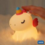 A glowing Sitting Unicorn Silicone Night Lamp with a colorful horn and pink wings on a pink background. - view 4