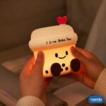 A glowing Boba Tea Silicone Night Lamp with a smiley face and heart topper sitting next to two macarons. - view 2