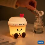 A glowing Boba Tea Silicone Night Lamp with a smiley face and heart topper sitting next to two macarons. - view 3
