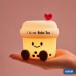 A glowing Boba Tea Silicone Night Lamp with a smiley face and heart topper sitting next to two macarons. - view 4