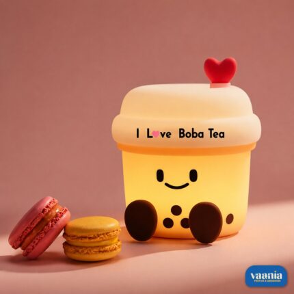 A glowing Boba Tea Silicone Night Lamp with a smiley face and heart topper sitting next to two macarons.