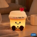 A glowing Boba Tea Silicone Night Lamp with a smiley face and heart topper sitting next to two macarons. - view 6