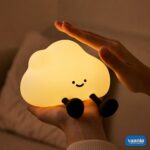 A glowing warm yellow One Cloud Silicone Night Lamp with a smiling face nestled in soft white cotton stuffing. - view 3