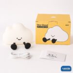 A glowing warm yellow One Cloud Silicone Night Lamp with a smiling face nestled in soft white cotton stuffing. - view 5