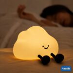A glowing warm yellow One Cloud Silicone Night Lamp with a smiling face nestled in soft white cotton stuffing. - view 2