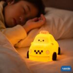 A glowing yellow Taxi Silicon Night Lamp with a smiling face on the windshield and black wheels. - view 2