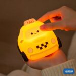 A glowing yellow Taxi Silicon Night Lamp with a smiling face on the windshield and black wheels. - view 3