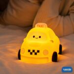 A glowing yellow Taxi Silicon Night Lamp with a smiling face on the windshield and black wheels. - view 4