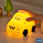 A glowing yellow Taxi Silicon Night Lamp with a smiling face on the windshield and black wheels. - view 5