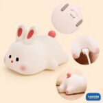 A glowing Rabbit Silicone Night Lamp with pink ears and a red tail sitting on a soft surface. - view 3