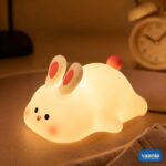 A glowing Rabbit Silicone Night Lamp with pink ears and a red tail sitting on a soft surface.