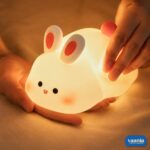 A glowing Rabbit Silicone Night Lamp with pink ears and a red tail sitting on a soft surface. - view 4