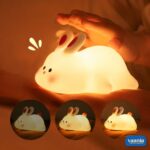 A glowing Rabbit Silicone Night Lamp with pink ears and a red tail sitting on a soft surface. - view 5
