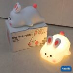 A glowing Rabbit Silicone Night Lamp with pink ears and a red tail sitting on a soft surface. - view 6