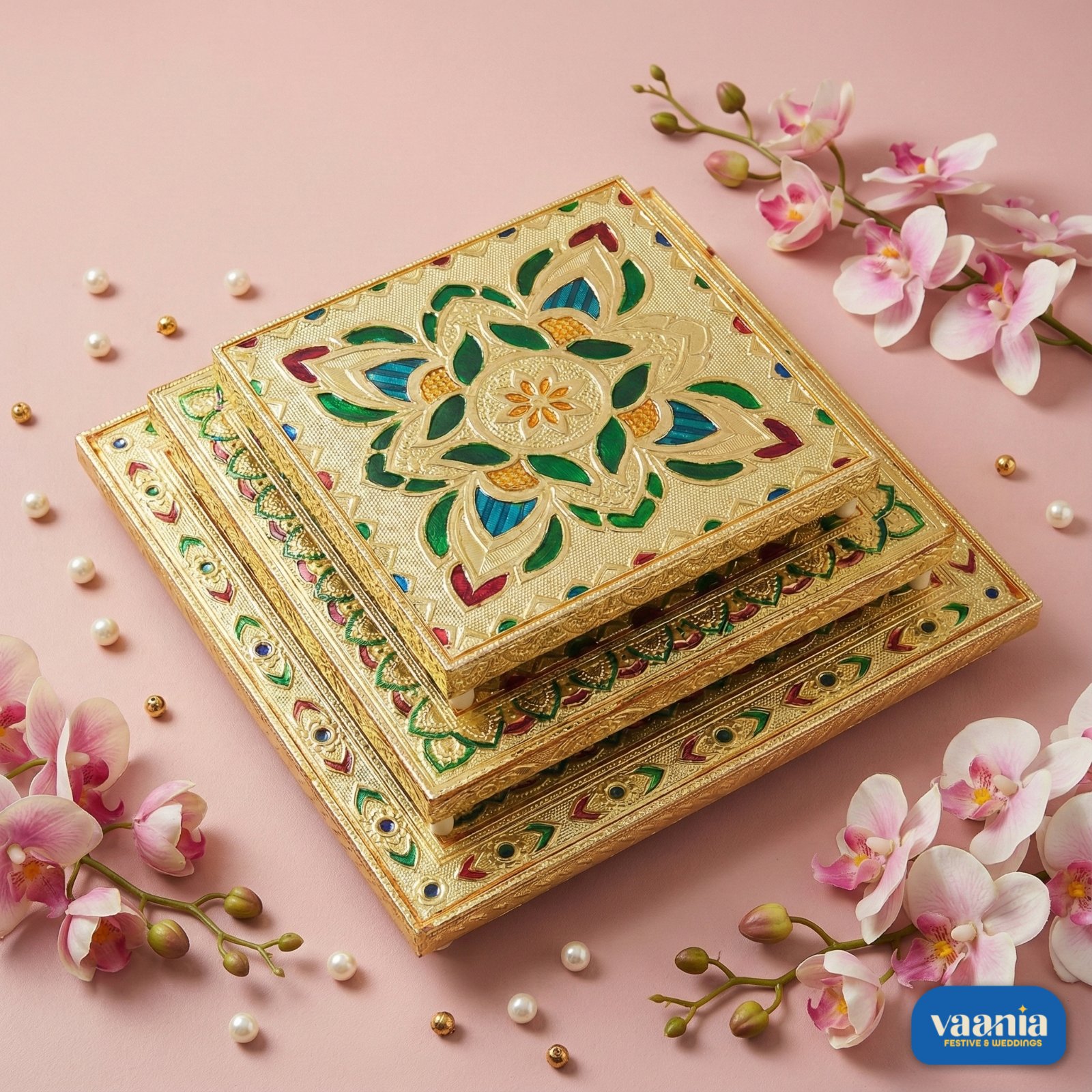 Vaania Big Square Chowki for Puja A stack of three Big Square Chowkis with gold finish and floral enamel patterns on a pink background.
