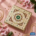 A square White Chowki with gold, red, and green intricate patterns on a pink fabric background with pearls.
