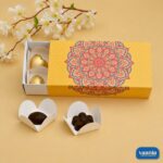 A yellow Sliding Cavity Box with a red and blue mandala design holding gold-wrapped chocolates and petal inserts.