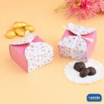 Two pink and floral Multi Purpose Boxes with white ribbons next to chocolates and golden sweets.