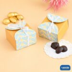 Two yellow Multi Purpose Boxes with blue patterned lids and white ribbons next to gold and dark chocolates.