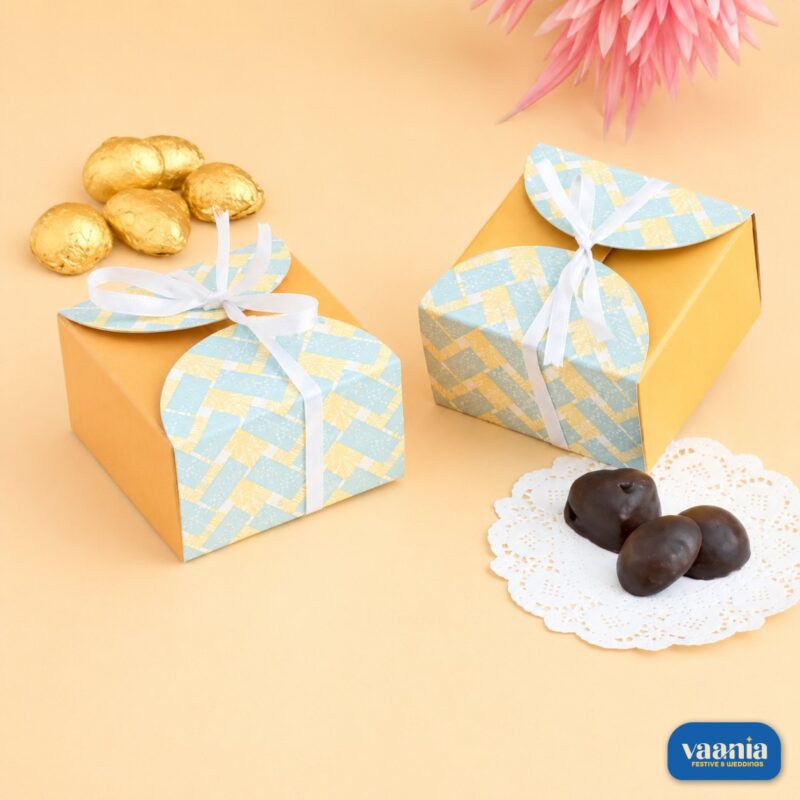 Two yellow Multi Purpose Boxes with blue patterned lids and white ribbons next to gold and dark chocolates.