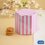 A pink and white striped hexagonal Multi Purpose Box with a clear handle next to a stack of cookies.