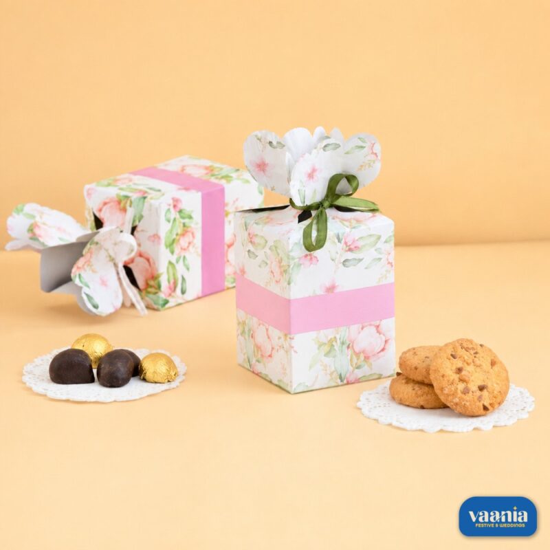 Two floral pattern multi-purpose boxes with pink bands, green ribbons, chocolates, and cookies on a beige background.