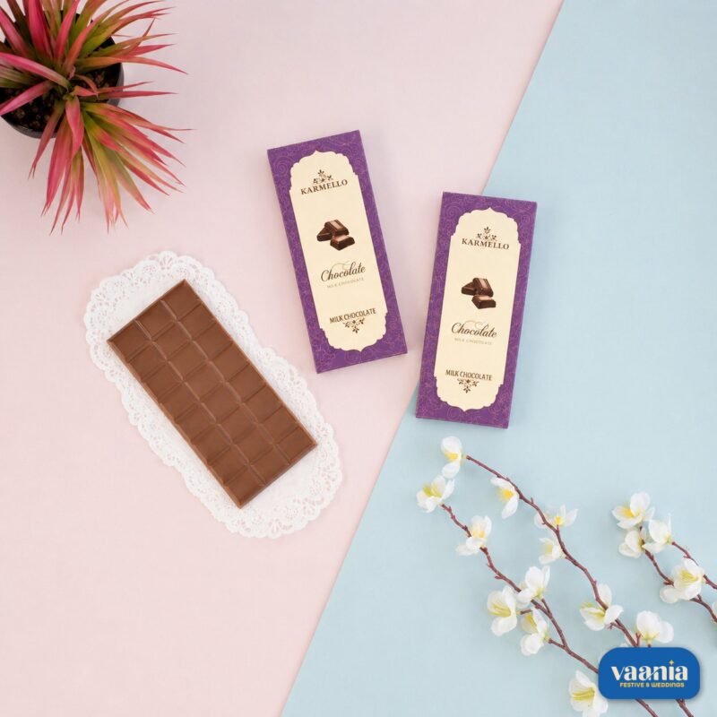 Two purple Karmello milk chocolate bar boxes next to an unwrapped chocolate bar on a white lace doily.