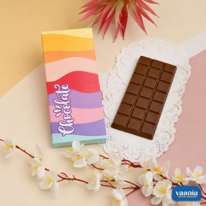 A milk chocolate bar next to a colorful wavy patterned Chocolate Bar Box with floral accents.