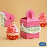 A pink chevron patterned Multi Purpose Box with white rope handles sitting next to a frosted cupcake.