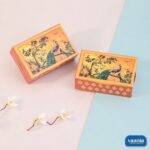 Two orange Multi Purpose Boxes featuring turquoise peacock illustrations on a floral background with side diamond patterns.