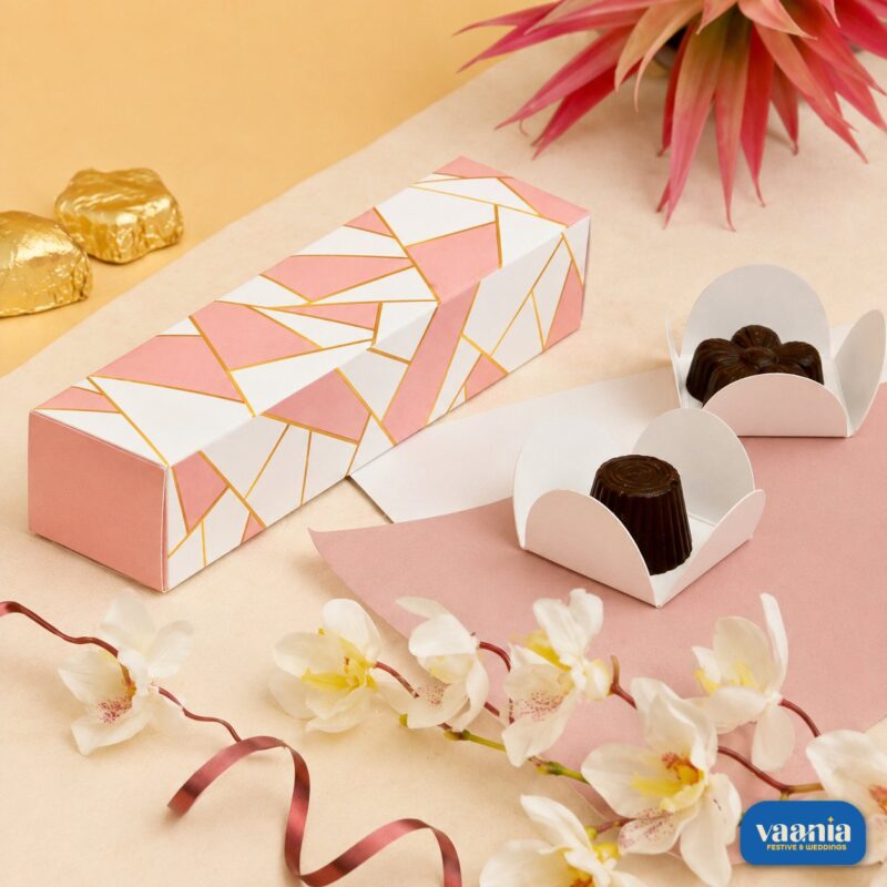 A pink and white geometric 4 cavity box displayed with dark chocolates in white liners and floral accents.