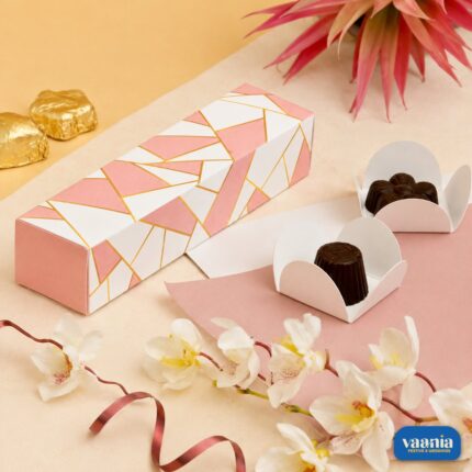 A pink and white geometric 4 cavity box displayed with dark chocolates in white liners and floral accents.