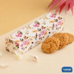 A white long rectangular Multi Purpose Box with pink and yellow floral patterns next to three brown cookies.