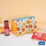 A floral print Hamper Box featuring yellow rope handles, styled with rose sharbat and savory snack packs.