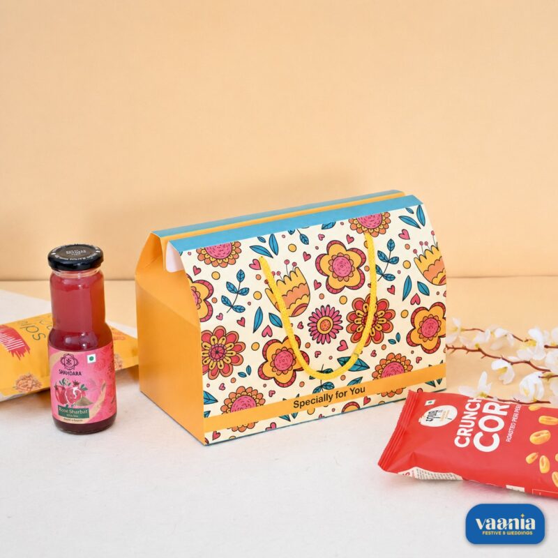 A floral print Hamper Box featuring yellow rope handles, styled with rose sharbat and savory snack packs.