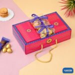 A pink and blue Hamper Tray with Boxes Compartments filled with sweets and tied with purple ribbons on a pastel desk.