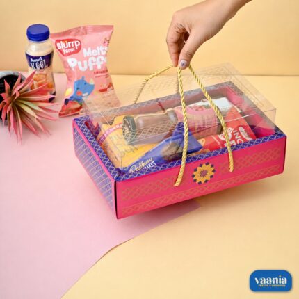 A pink patterned Hamper Tray with a clear PVC lid filled with snacks and held by golden rope handles.