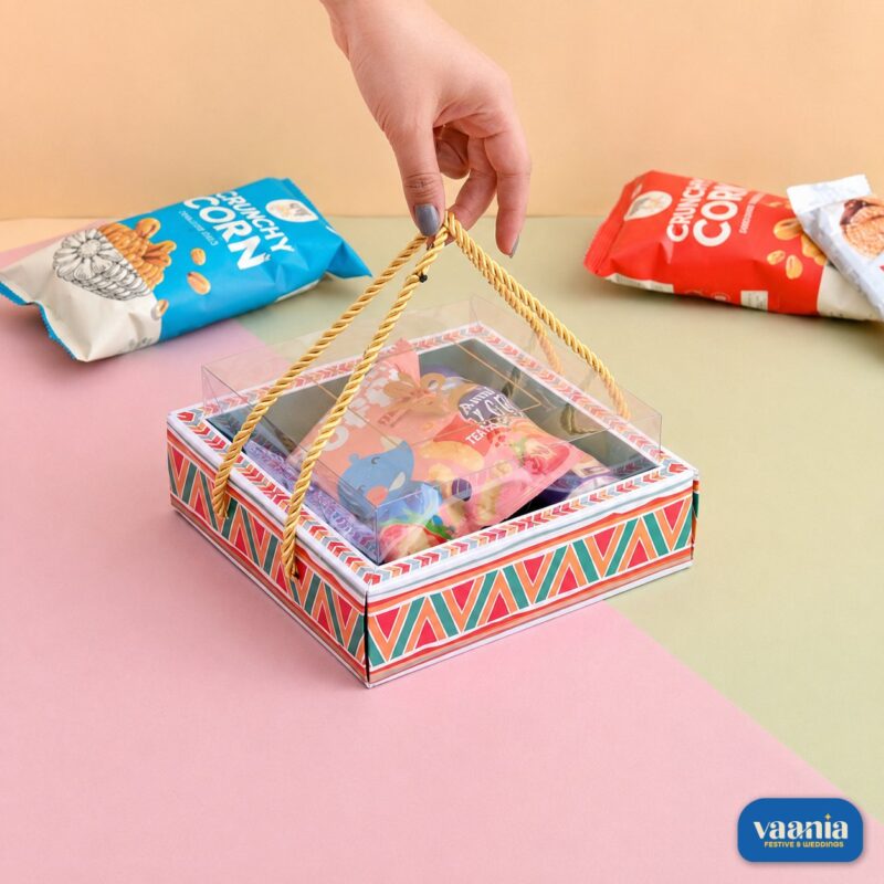 A hand lifting a colorful geometric print Hamper Tray with a clear PVC lid and gold rope handles.