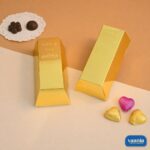 Two shiny gold brick boxes shaped like bullion alongside assorted heart-shaped and dark chocolates.
